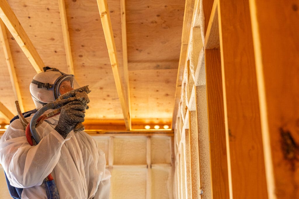 Worker applying spray foam insulation in attic.