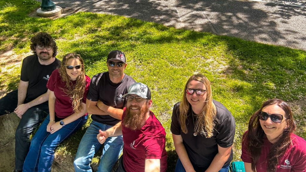 Group of six people sitting outside on grass.