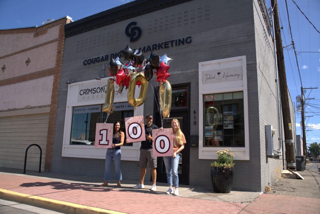 Three people celebrate milestone with 100 balloon display.