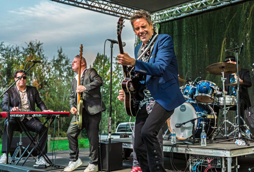 Band performing live on outdoor stage with instruments.