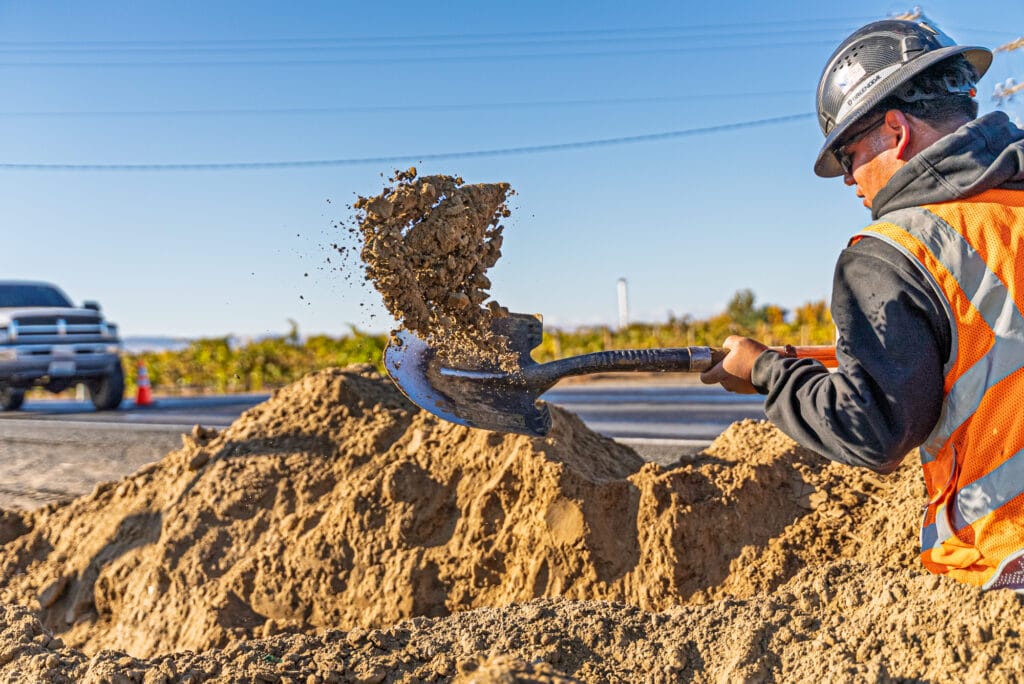 Construction worker shoveling dirt roadside.