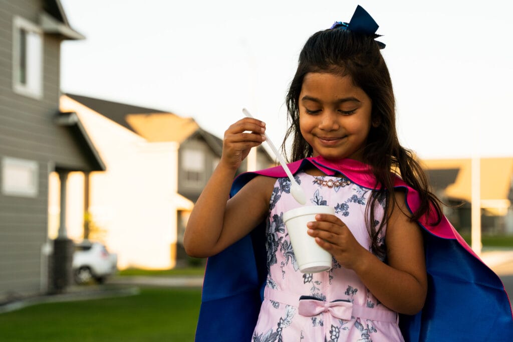 Girl in superhero cape eating ice cream outside