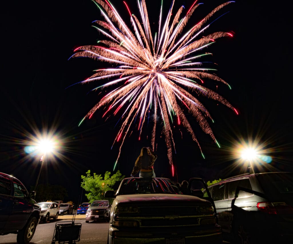 Fireworks exploding over parked cars at night.