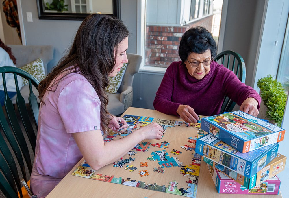 Two women assembling a jigsaw puzzle on a table.