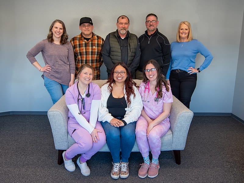 Group of eight smiling healthcare professionals posing indoors.