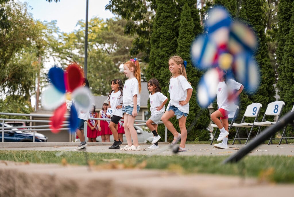 Children dancing outdoors with colorful pinwheels.