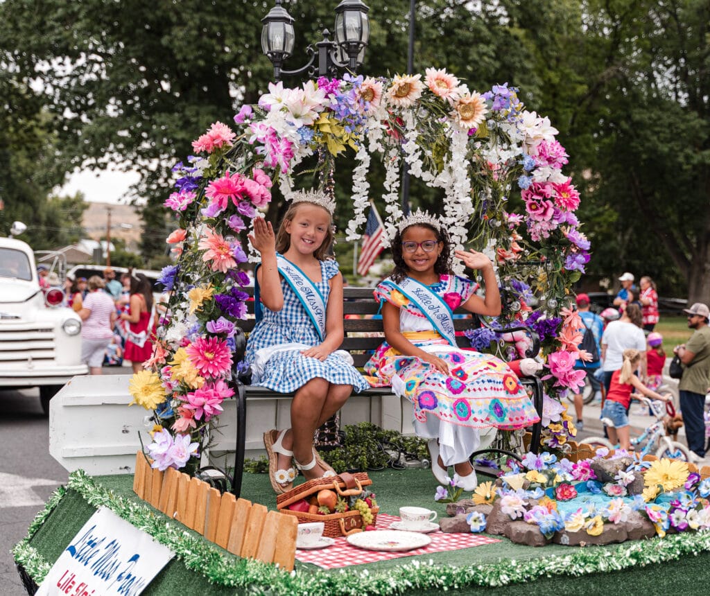 Girls in colorful dresses on a parade float waving.