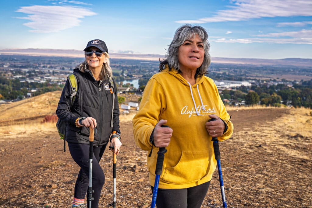 Women hiking with trekking poles on a scenic trail.