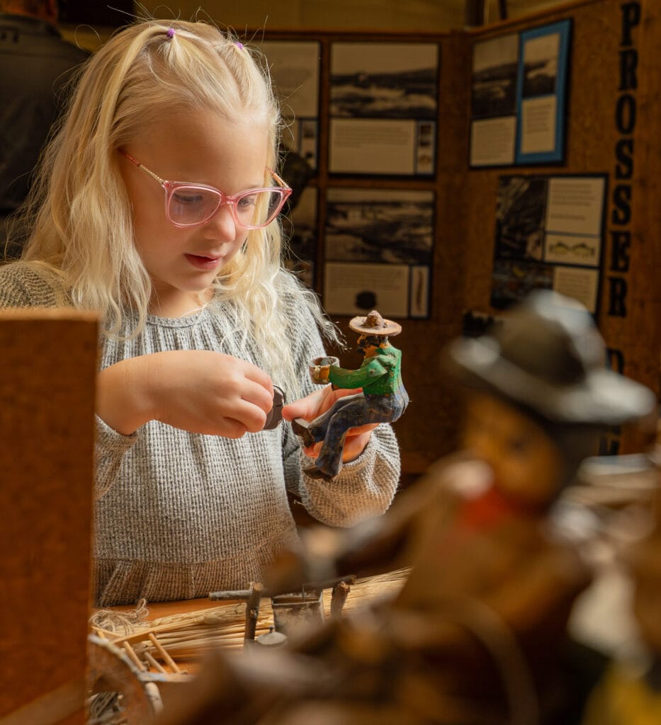 Girl with glasses examining clay figure indoors.