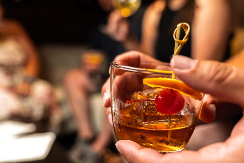 Hand holding cocktail with orange and cherry garnish