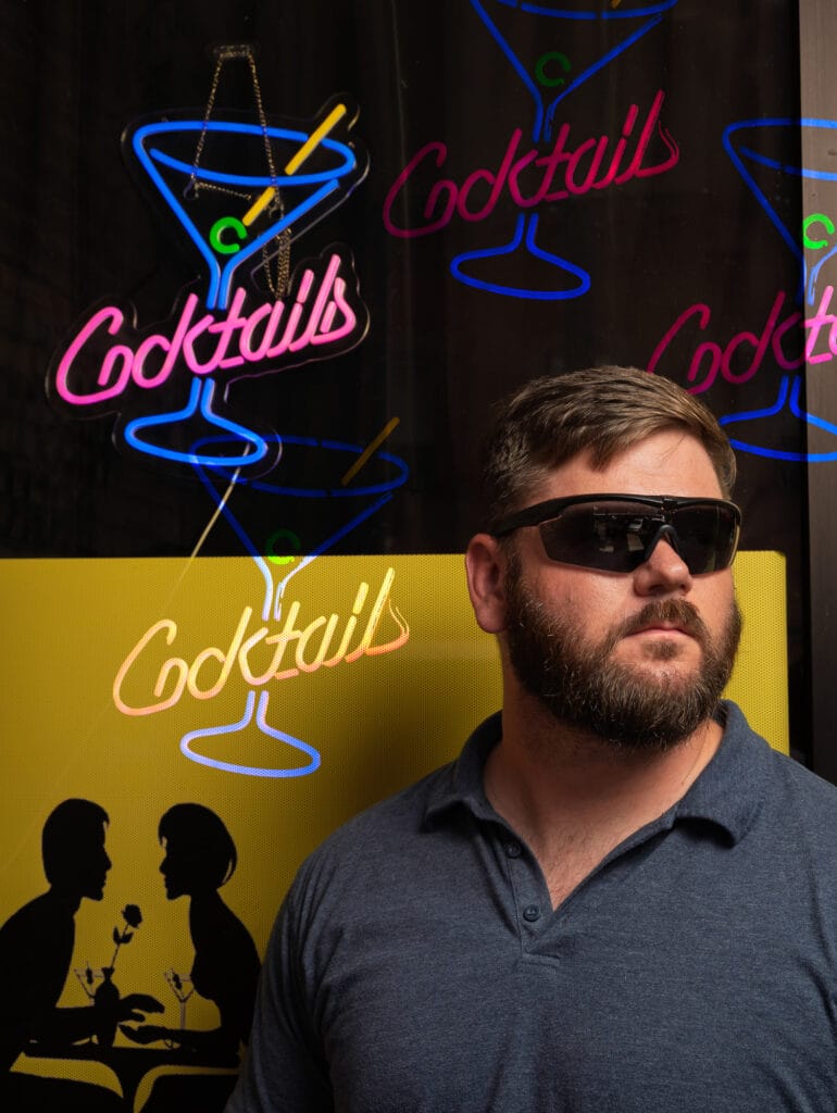 Man with sunglasses near cocktail neon signs.
