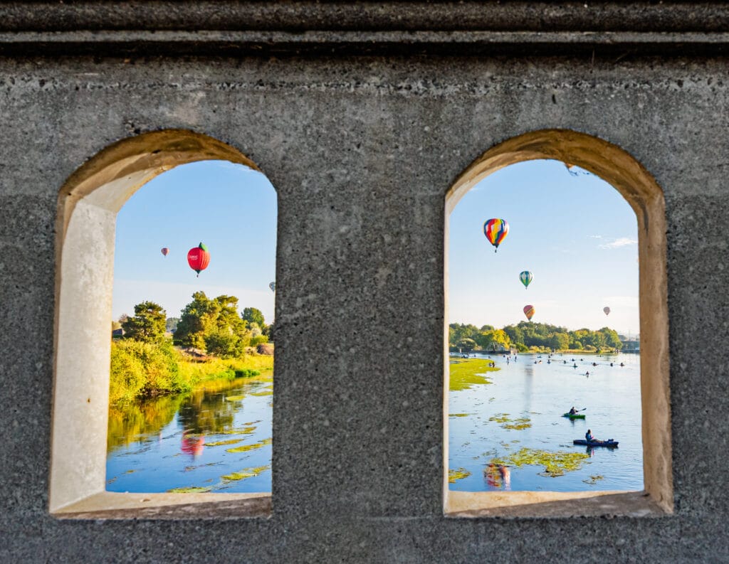 Hot air balloons over river, view through arch.