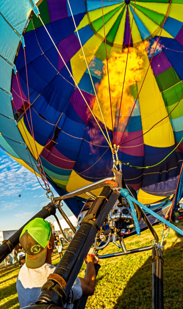 Person inflating colorful hot air balloon with flame.