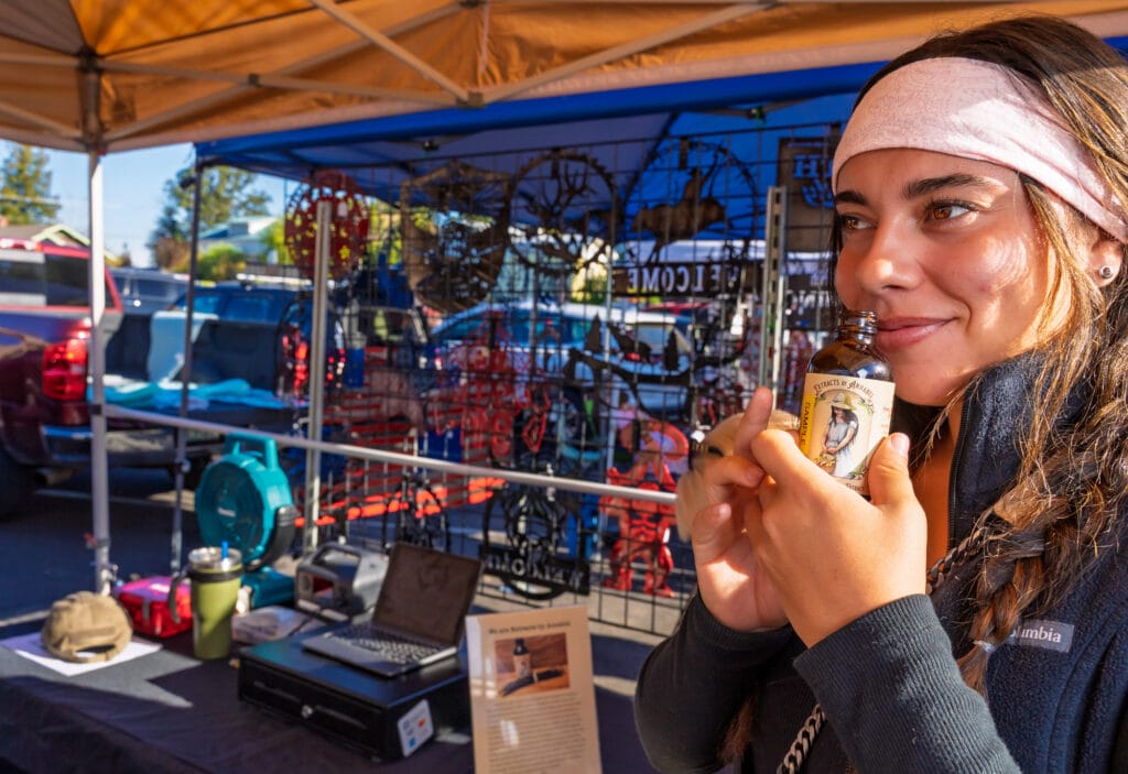 Woman enjoying a scented bottle at outdoor market.