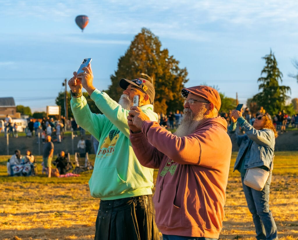 People photographing hot air balloon in field.