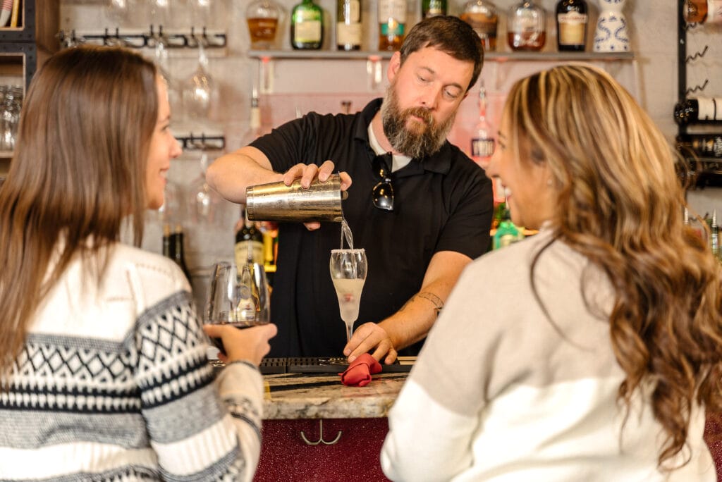 Bartender preparing drink for two women at bar.