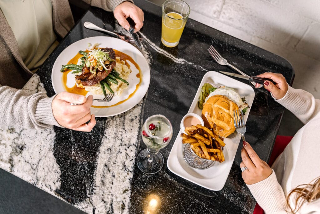 Two people dining with steak and burger meals.