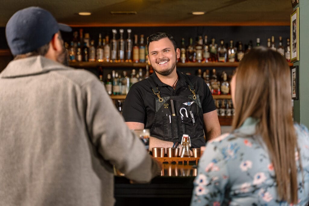 Bartender smiling, serving two customers at bar.