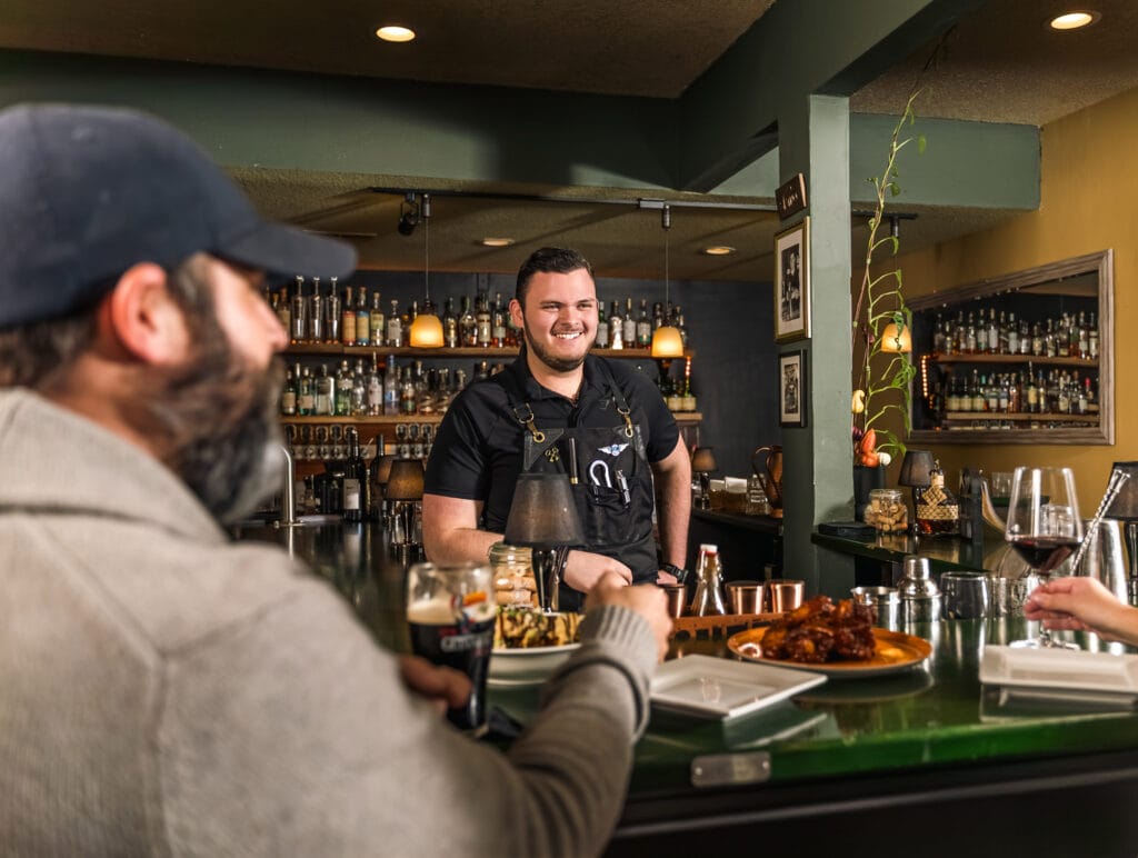 Smiling bartender serving drinks at a lively bar.
