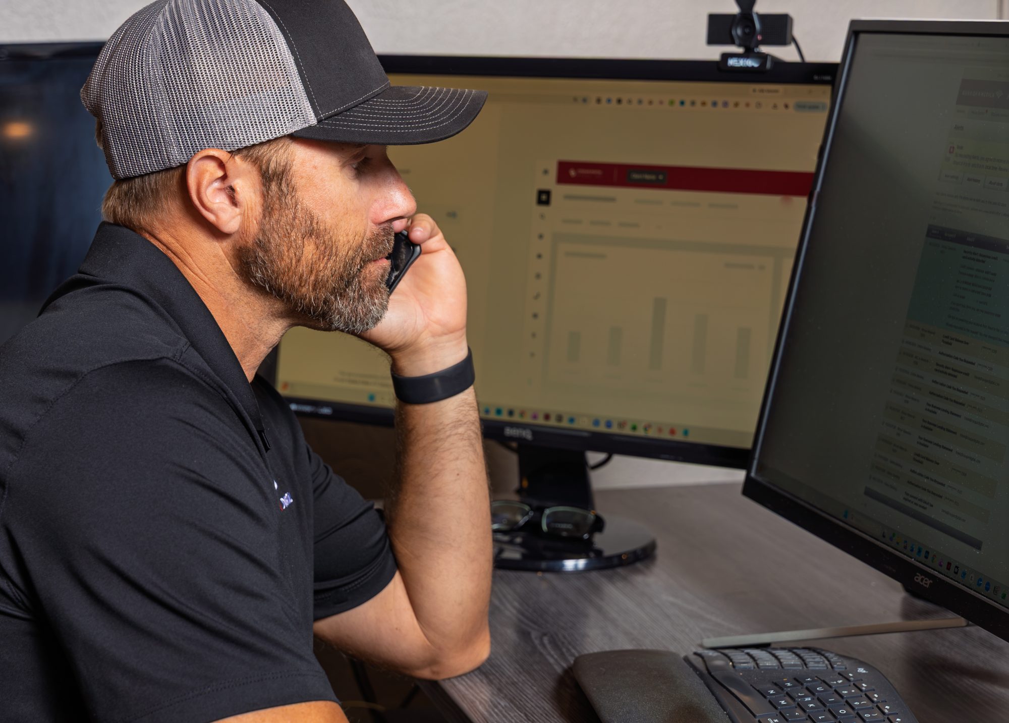 Man in cap talking on phone at dual monitor workstation