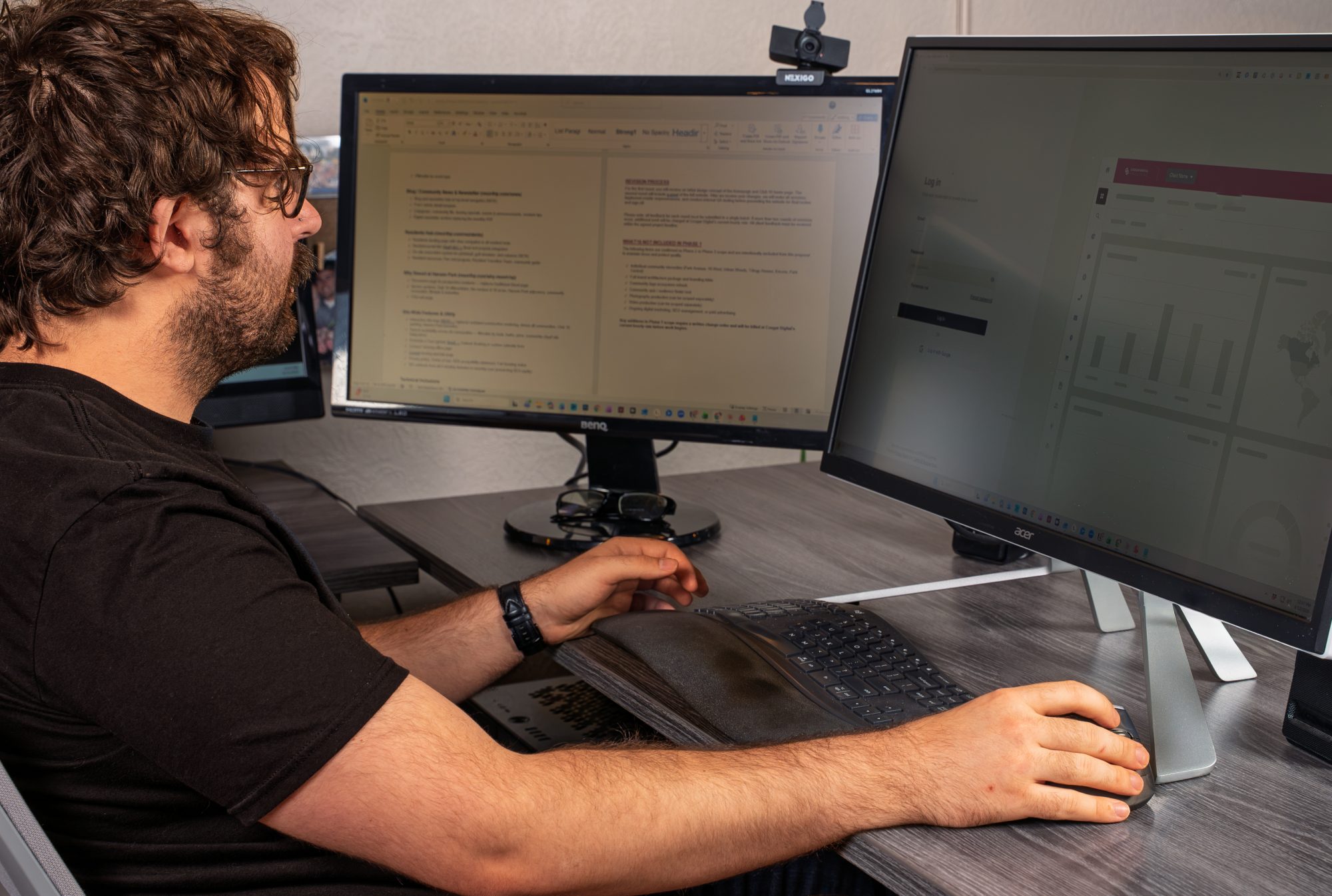 Man working at dual monitor computer setup with webcam