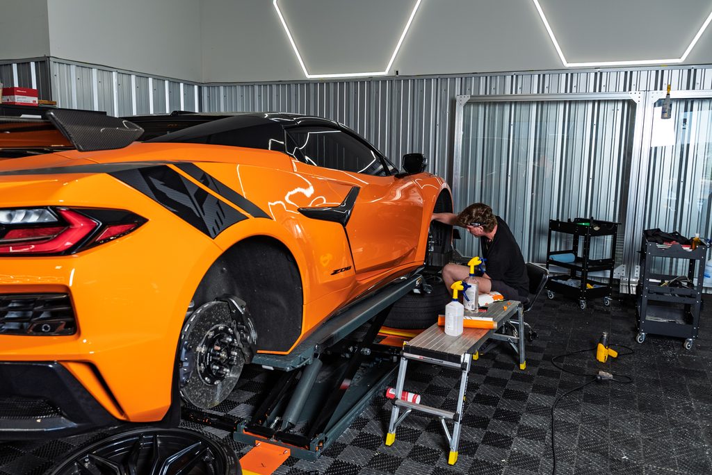 Technician detailing an orange Corvette Z06 on a lift