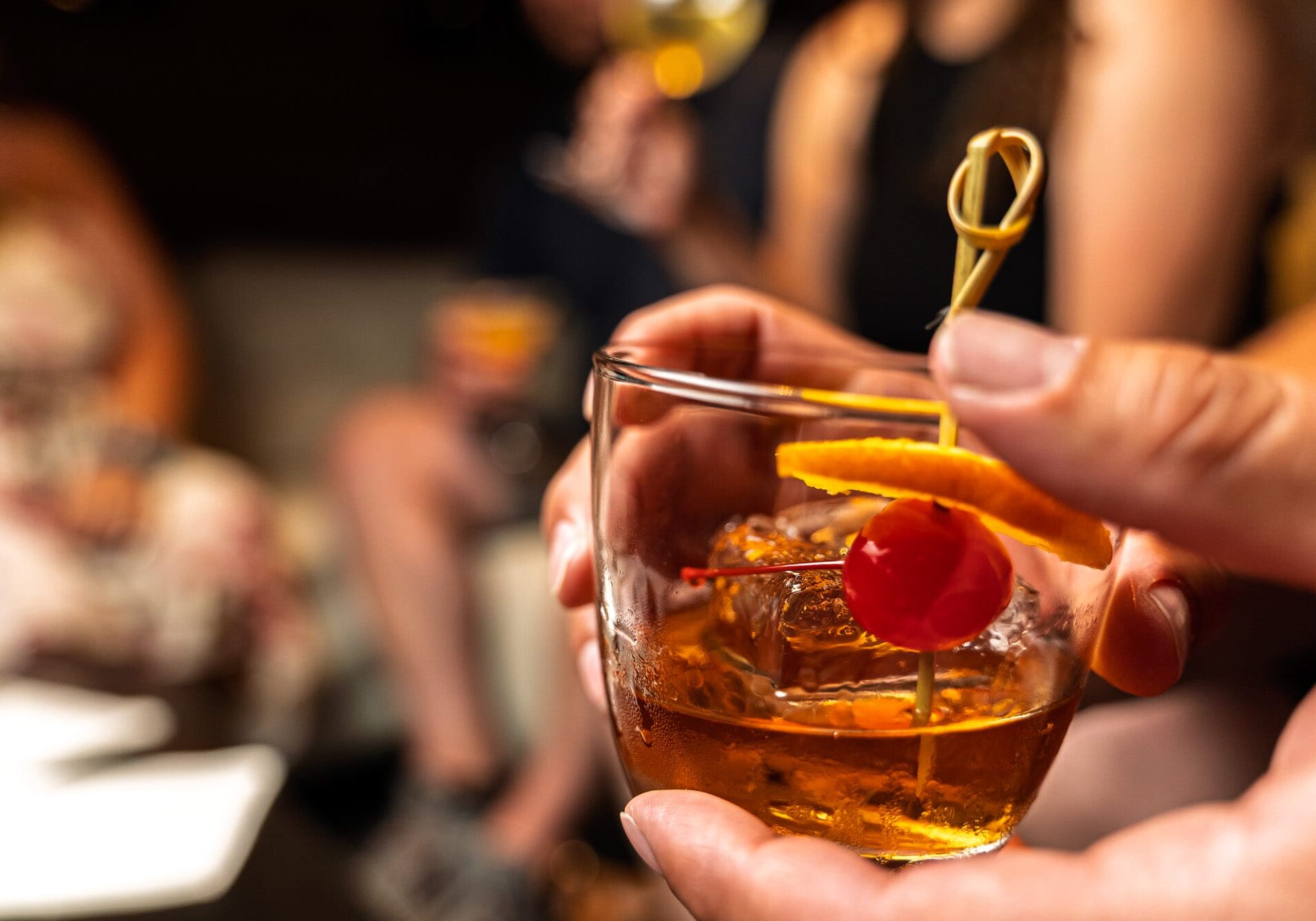 Hand holding cocktail with orange and cherry garnish