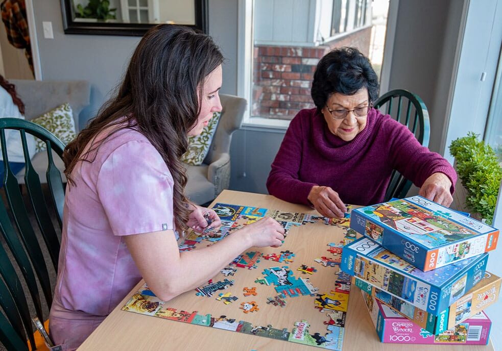 Two women assembling a jigsaw puzzle on a table.