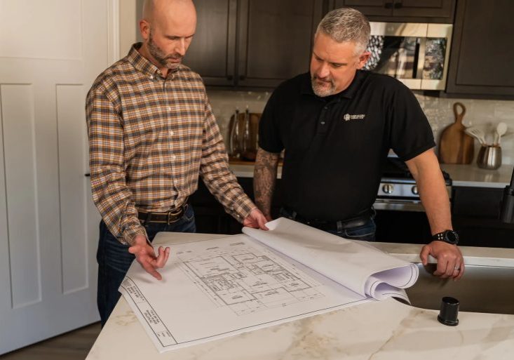 Two men reviewing house blueprints in kitchen
